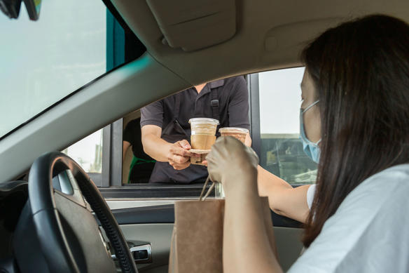 a woman wearing a mask receives food at a drive-through restaurant